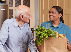 Home Care Worker woman helping senior man with groceries