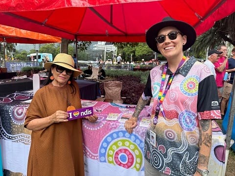 Two people standing in front of a booth with materials on the NDIS.