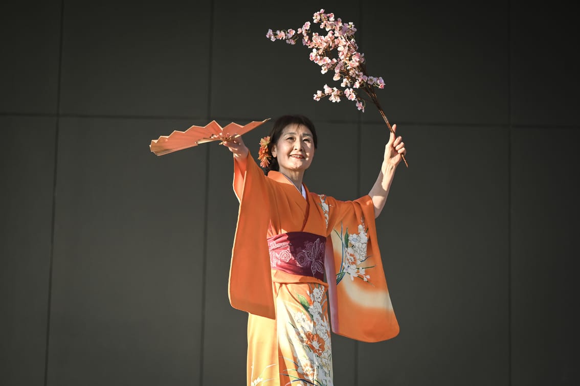 A woman performs on stage holding a fan in one hand and flowers in the other