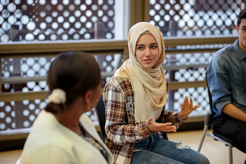 A multi-ethnic group of adults are studying together after class. They are in a university classroom taking continuing adult education classes.