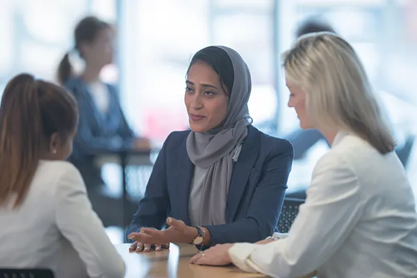 Diverse group of professional women collaborating in a workplace meeting seated at a table in a bright modern office