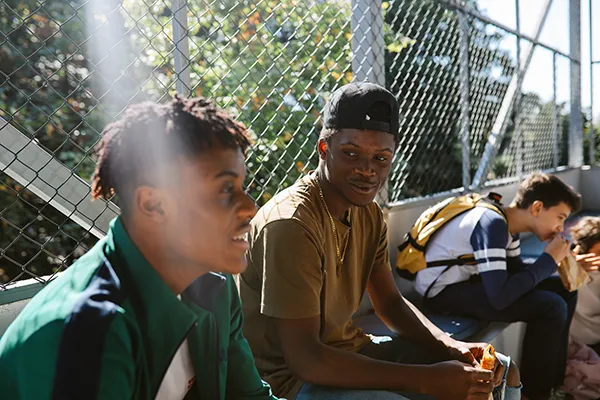 Two young males are sat talking on the back row of a community sports stand