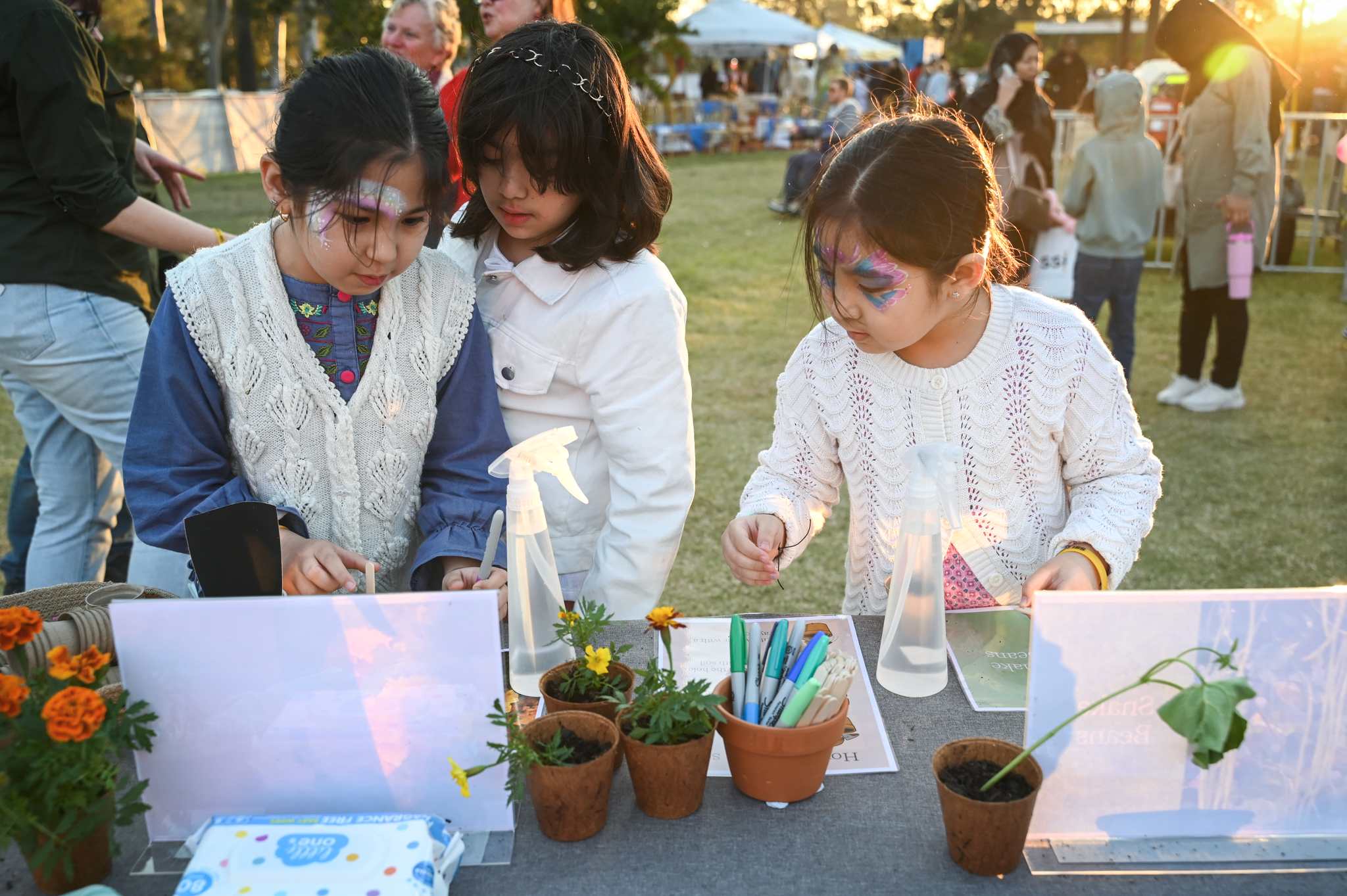 Three children with their face painted are engaging in a craft activity